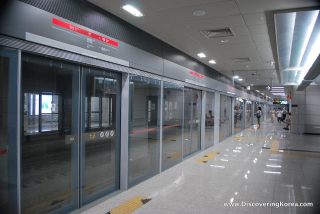 Inside Seoul's metro station, showing polished stone floors, with yellow markers at the glass doors to the left of the frame in front of the train tracks.