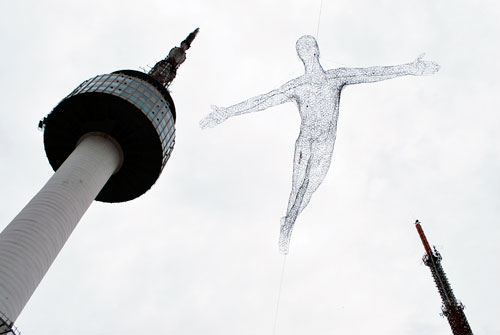 Seoul Tower to the left of the frame, in the center is a sketch of a man with his arms out, as though flying.