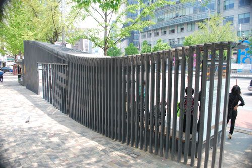 A bus stop made out of a curved metal railing with stone walkways either side, with trees in the background.