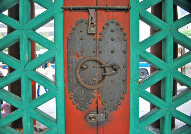 Close up of an ornate door, with turquoise carving on either side of red wood with slightly rusty metal locks and latches.