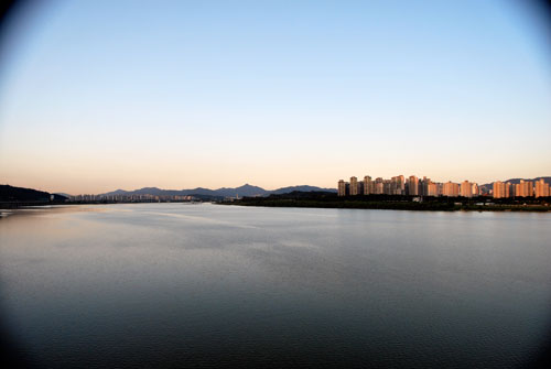 Wide angle view over the Hangang river with the city in the distance, soft evening light and mountains in the far background.