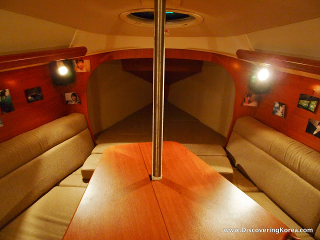 Interior of a yacht at Seoul marina. On either side are leather seats, with a central wooden table. The sides are walnut, with a pole going up to the ceiling.