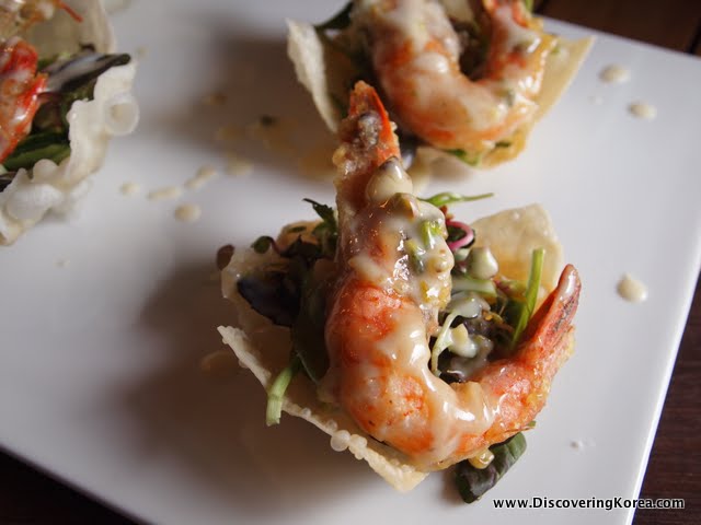 A close up of a white plate with shrimp on a crispy base, with green vegetables underneath.
