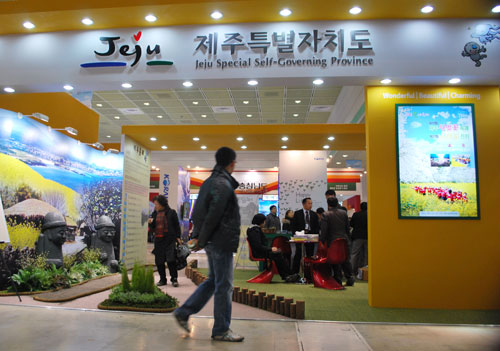 A man walks past an exhibit at the Korea Travel Expo, with bright pictures of landscapes on the walls, fake grass on the ground and a low fence.